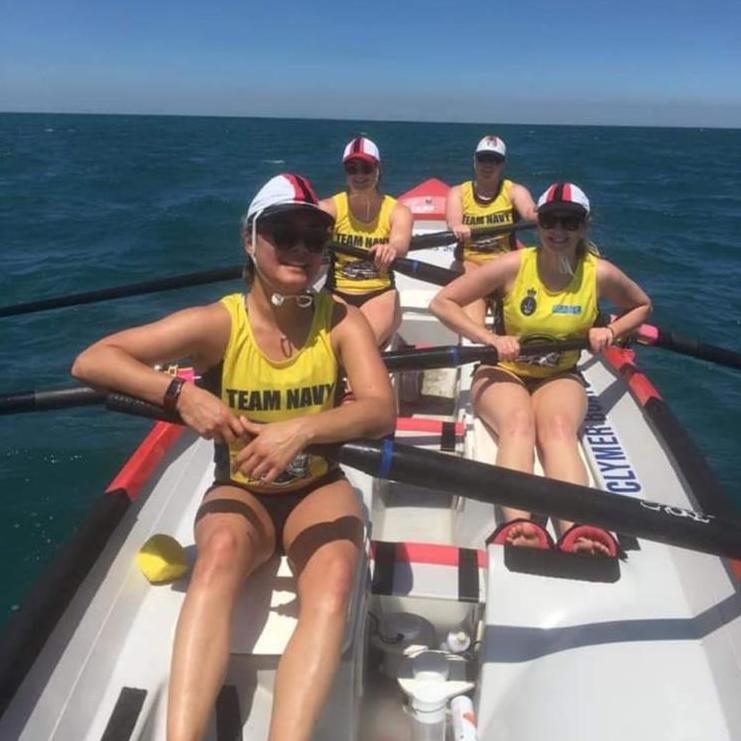 Kat, Nicole, and surf league rowing team in a boat on the water.