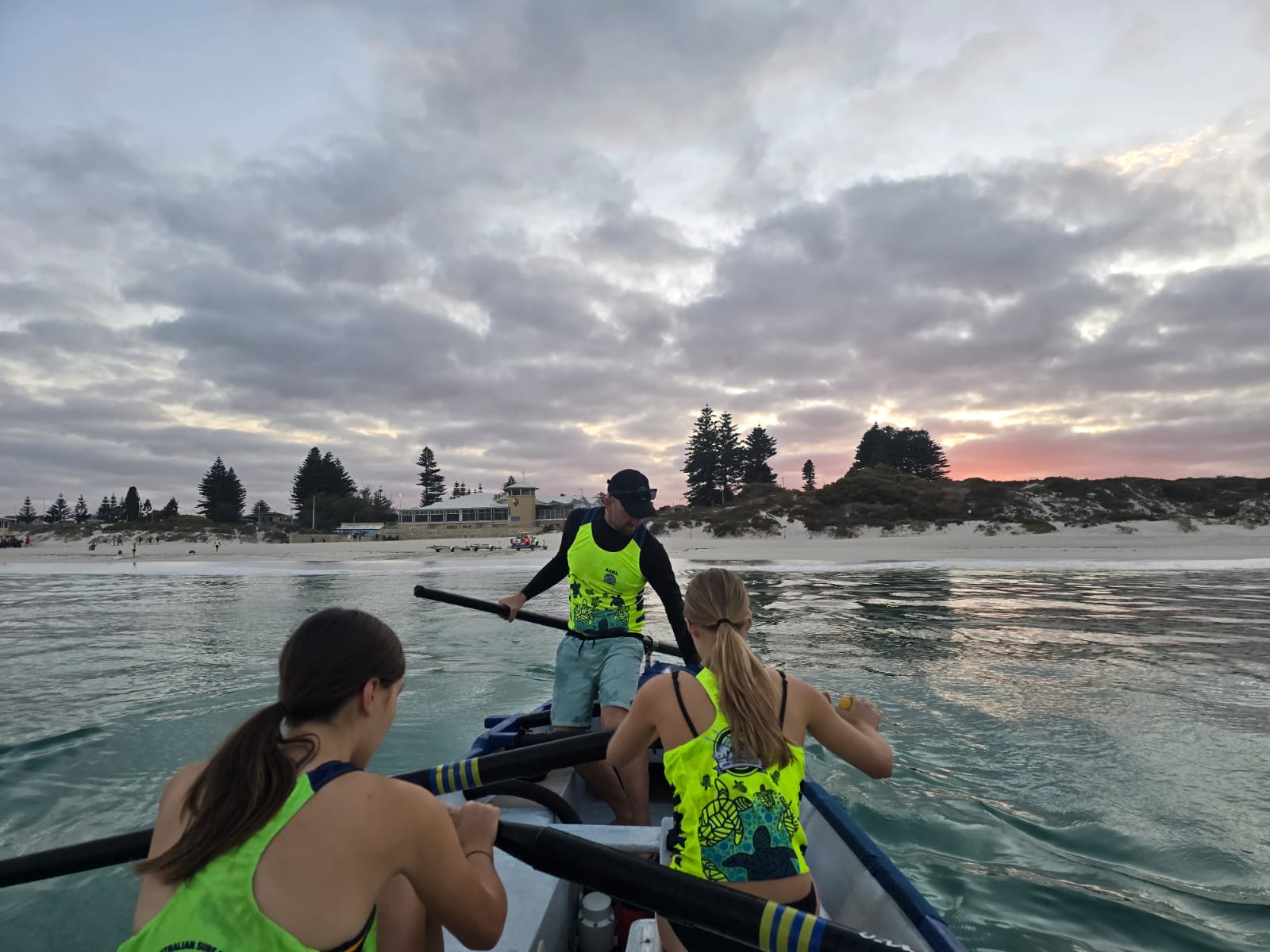 Three women rowing in a boat while wearing lime green sports tops